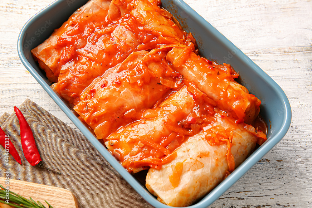 Baking dish with tasty stuffed cabbage rolls on light wooden background