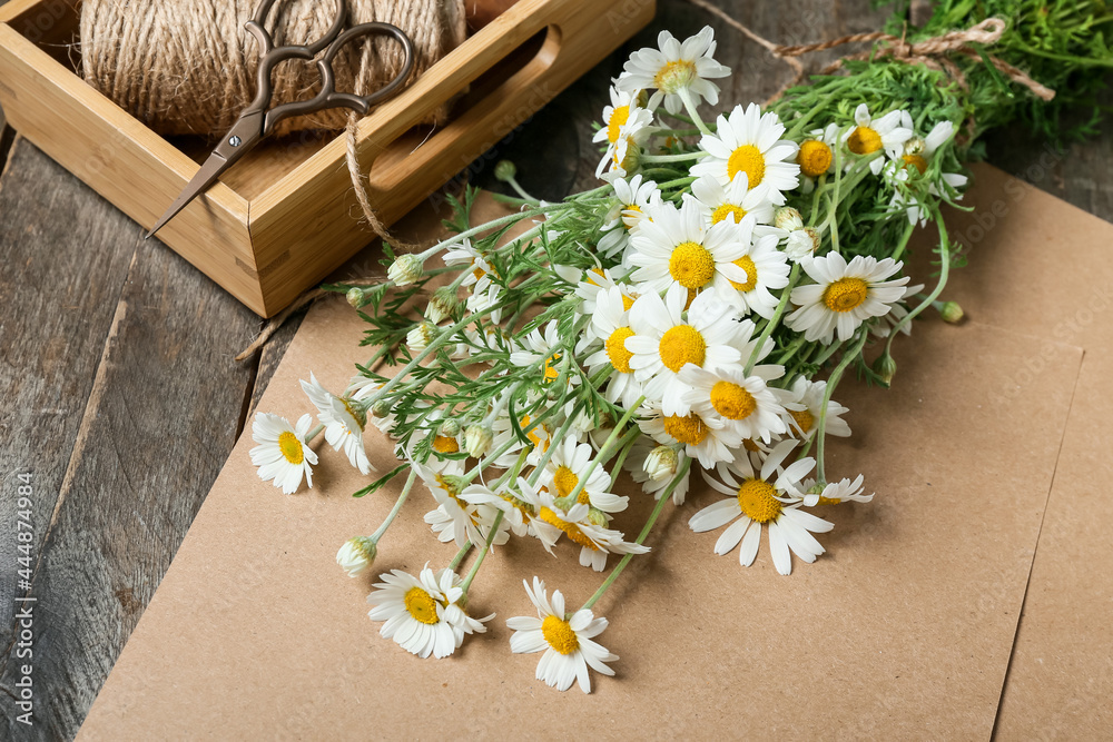 木质背景上美丽的洋甘菊花、剪刀、绳子和工艺纸的花束，特写