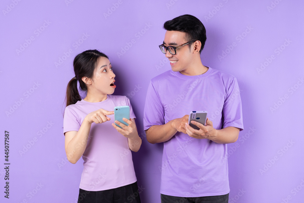 Young Asian couple using smartphone on purple background