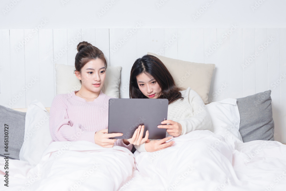 Two beautiful women lying on the bedside using a tablet