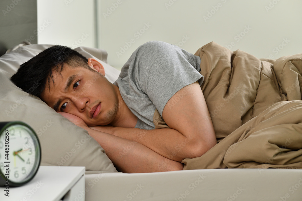 Depressed young Asian man lying in bed cannot sleep from insomnia