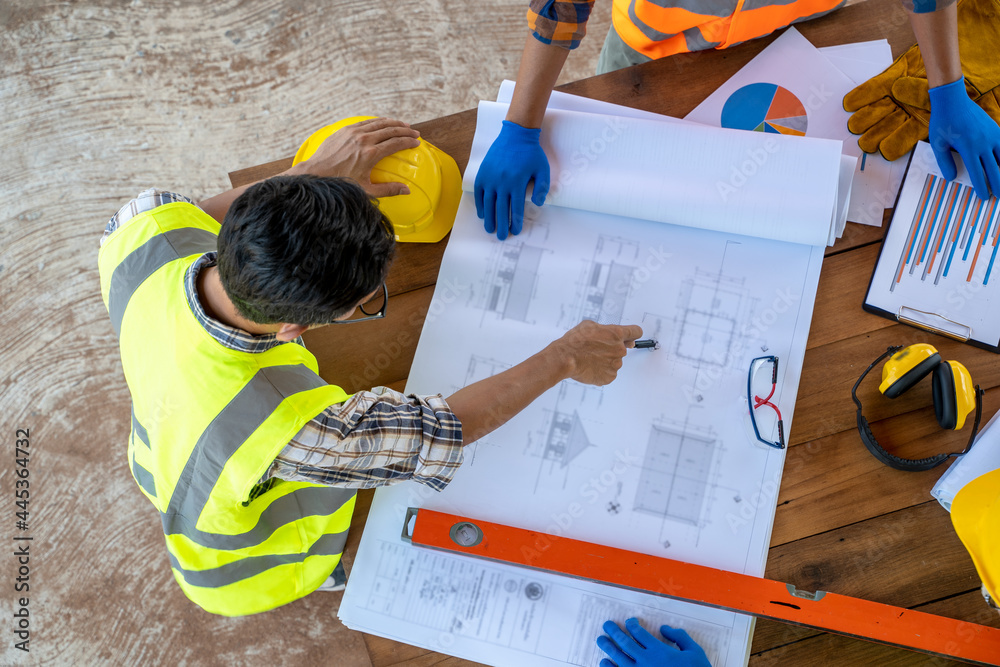 Top view of Engineers or architect holding a pen with drawings in construction on blueprints in cons