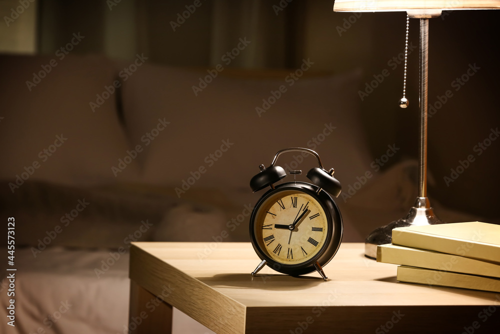 Alarm clock with books on table in bedroom at night