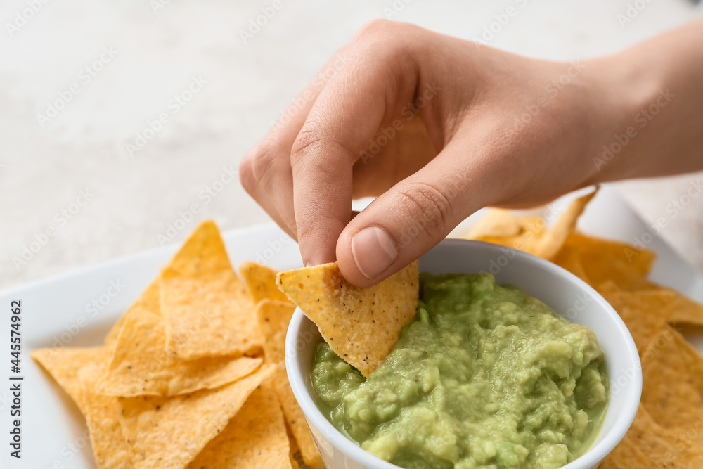 Woman eating tasty guacamole with nachos on light background, closeup