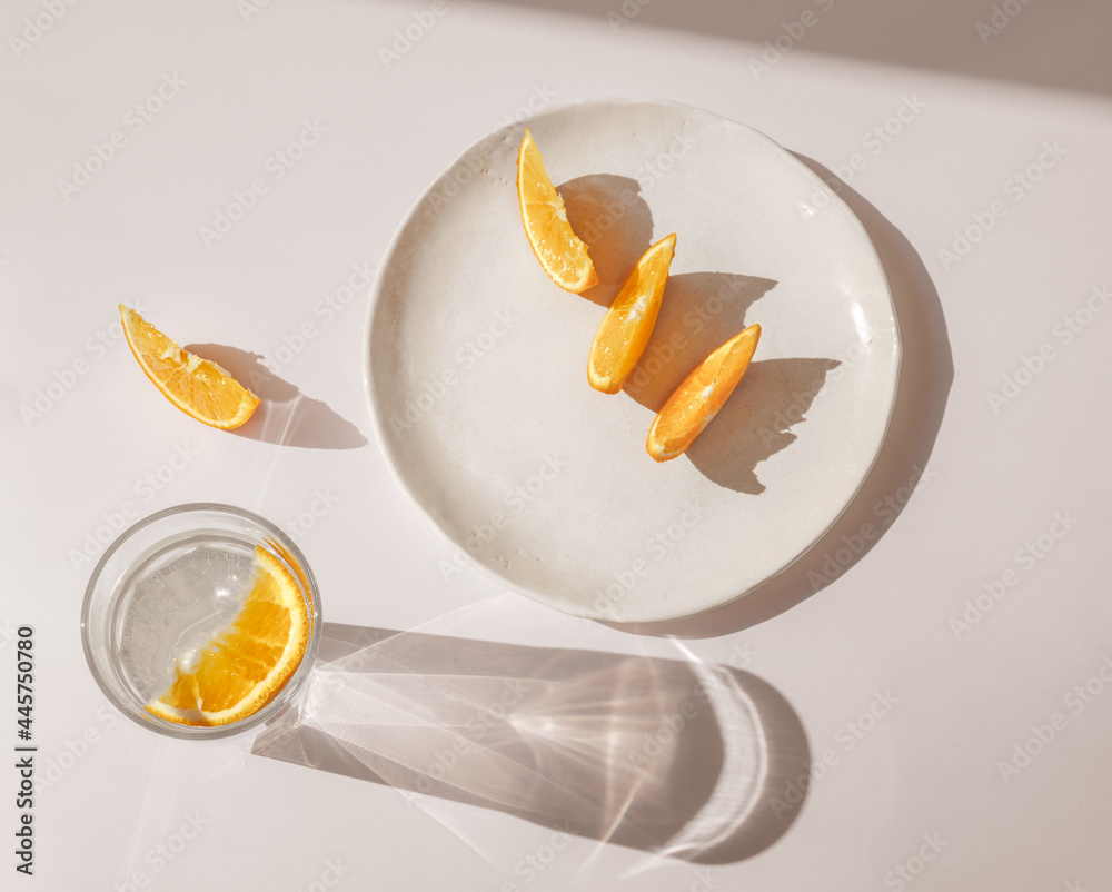 Sliced orange with glass of water and sharp shadows stands on light pink background. Top view flat l