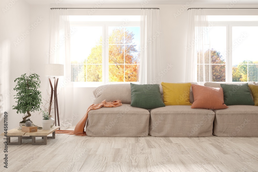 Stylish room in white color with sofa and autumn landscape in window. Scandinavian interior design. 