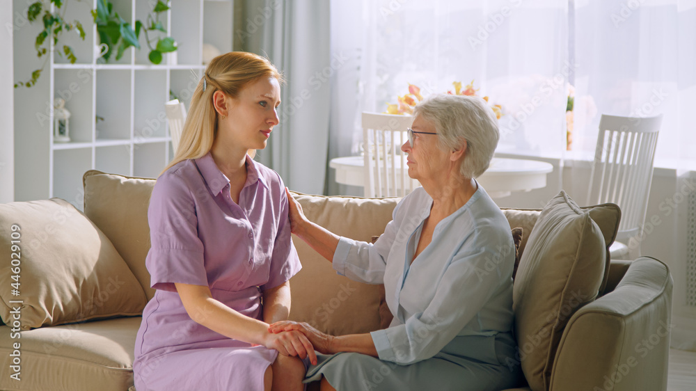 Elderly mother holding hand of young daughter on sofa at home