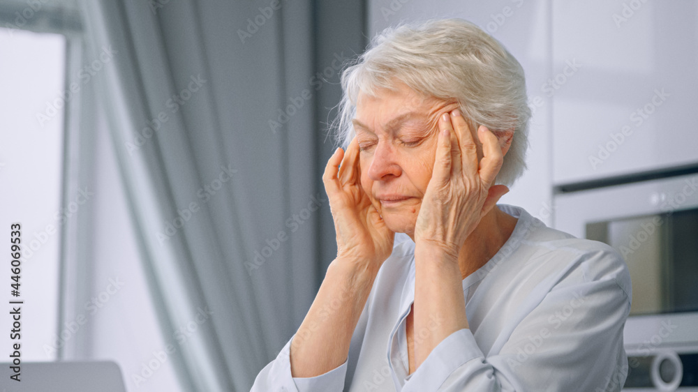 Old tired of work lady pensioner with short grey hair massages temples with hands