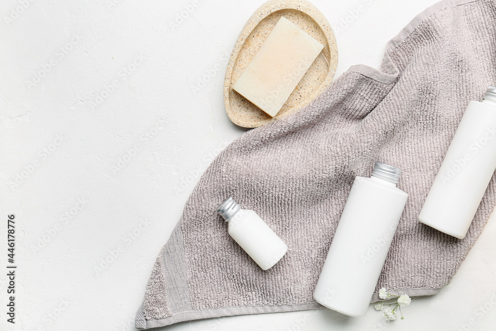 Bottles of cosmetic products, soap and towel on light background