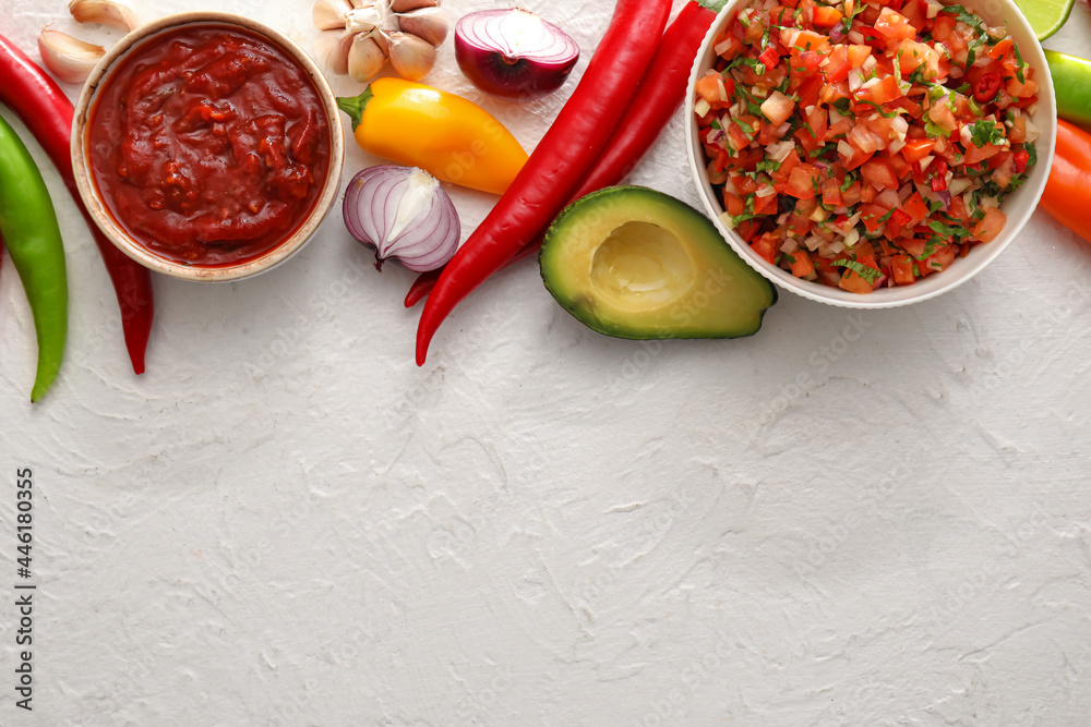 Bowls of tasty salsa sauces with products on white background