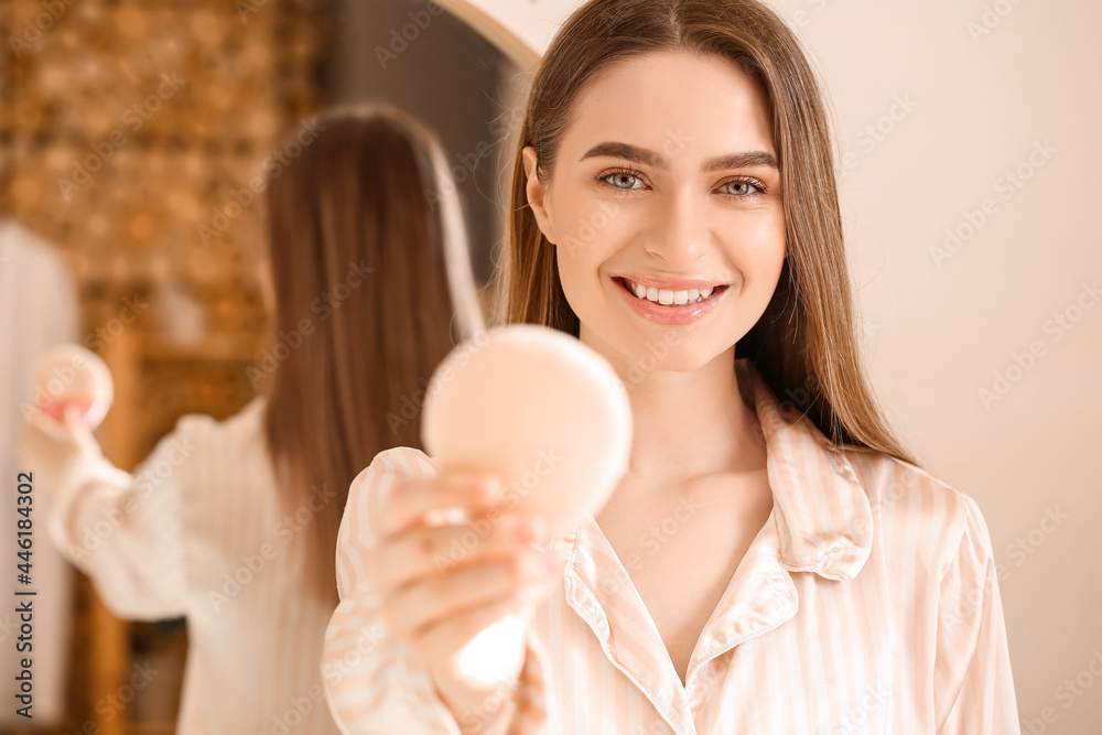 Beautiful young woman applying makeup in bathroom