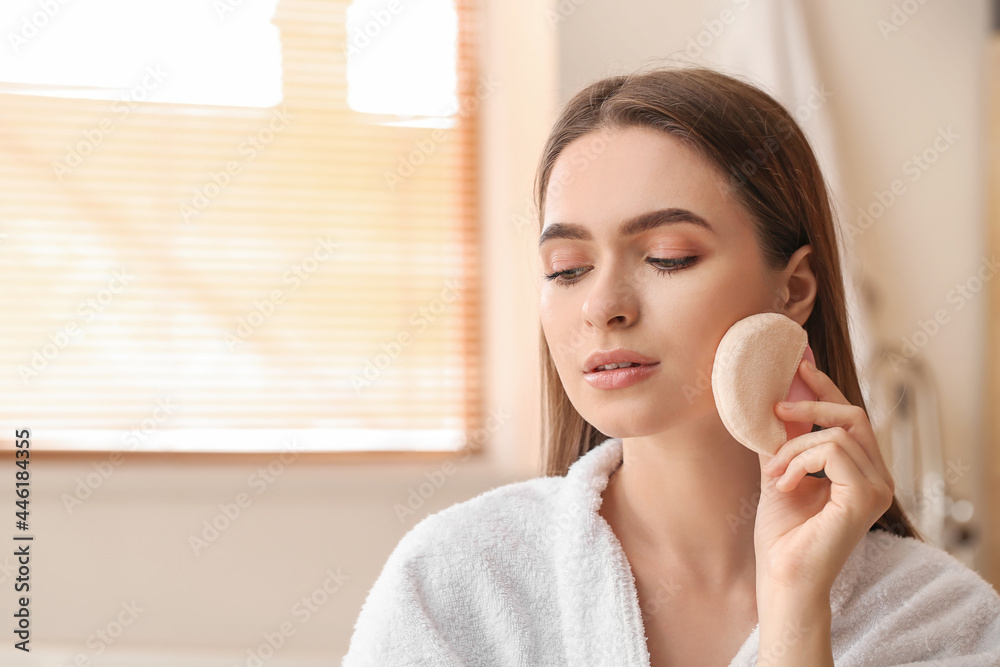 Beautiful young woman applying makeup in bathroom