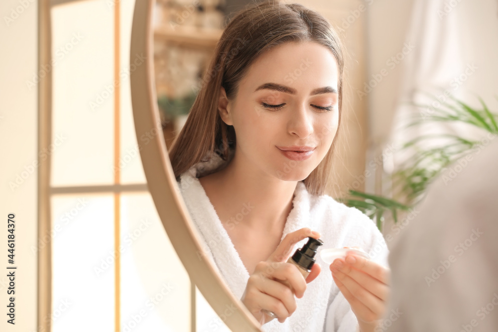 Beautiful young woman applying makeup in bathroom