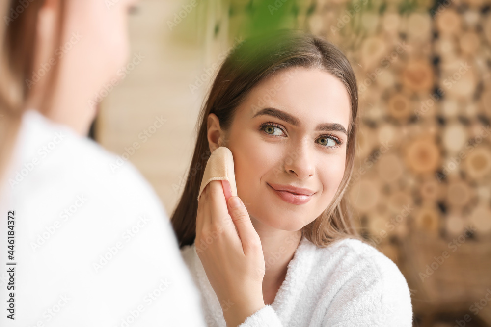 Beautiful young woman applying makeup in bathroom