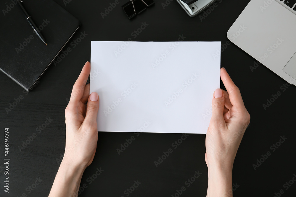 Woman holding blank sheet of paper on dark background