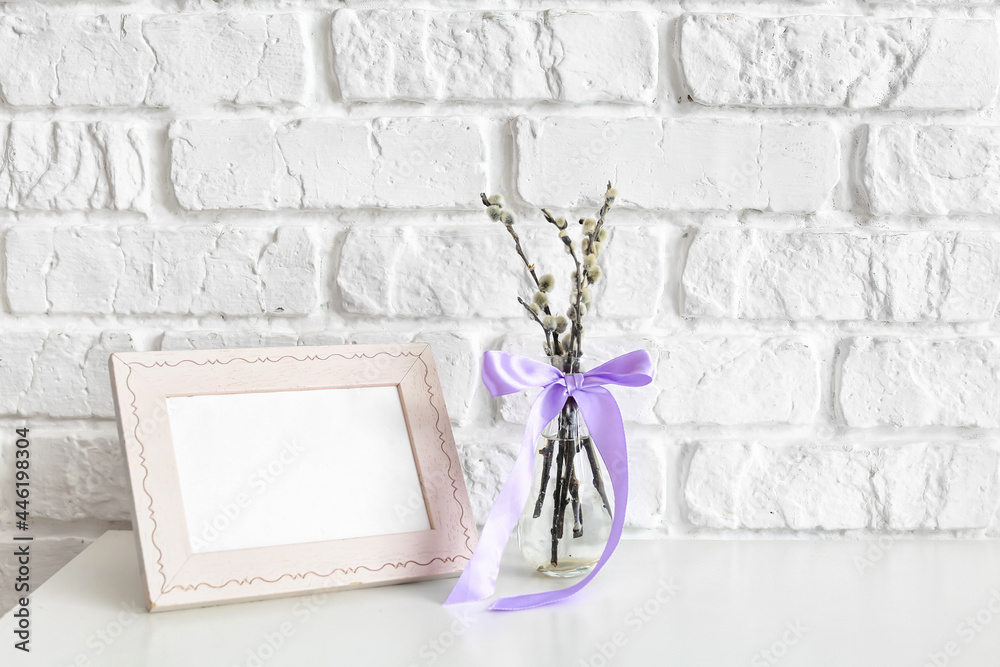 Willow branches with photo frame on table near brick wall