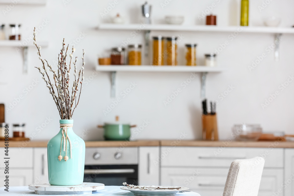 Vase with willow branches on table in dining room