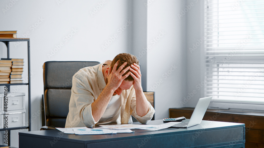 Upset financial director reads bank reports sitting at grey table