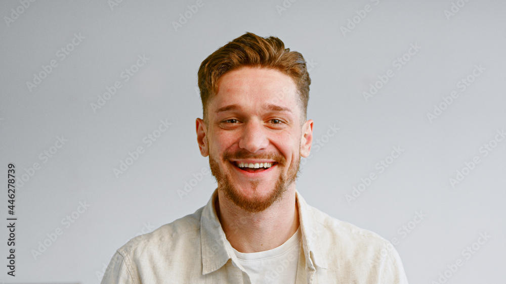 Portrait of serious bearded guy in yellow shirt looking straight and then smiling cheerfully