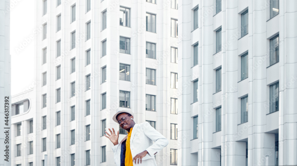 Amazed black guy in yellow t shirt and white suit dances contemporary dance against megalopolis offi