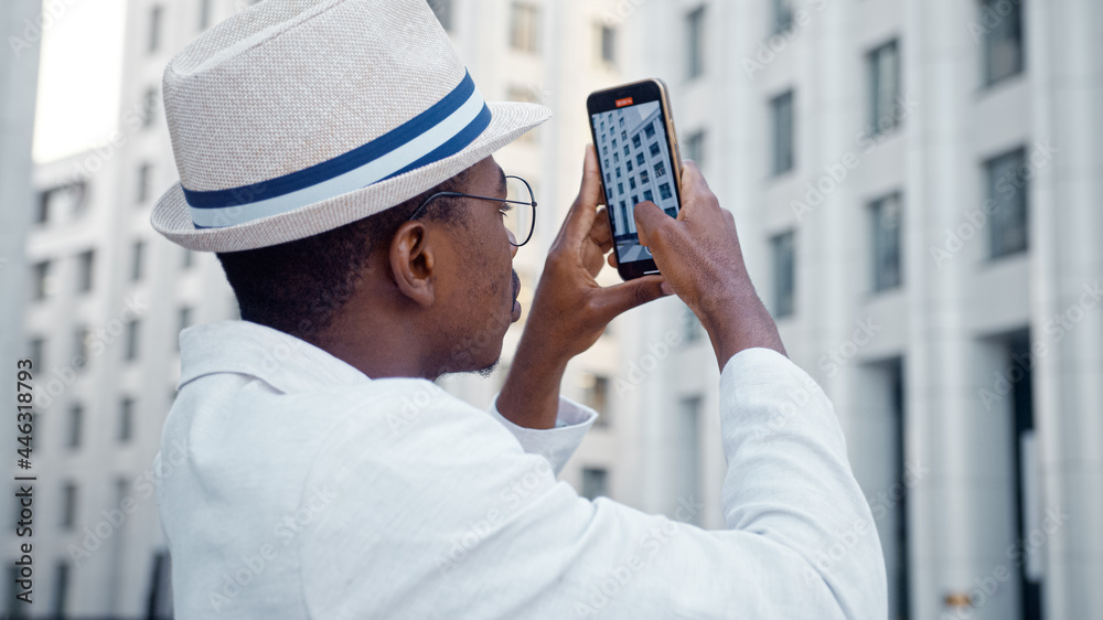 Black man tourist in white suit and glasses holds smartphone and films highrise megalopolis office b