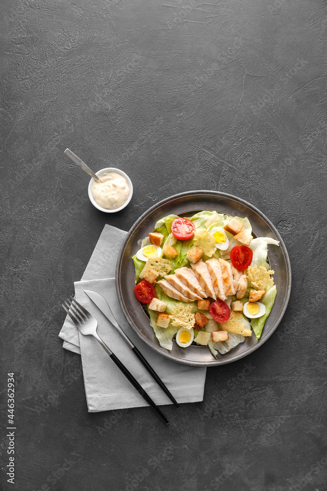 Plate with tasty Caesar salad and sauce on dark background