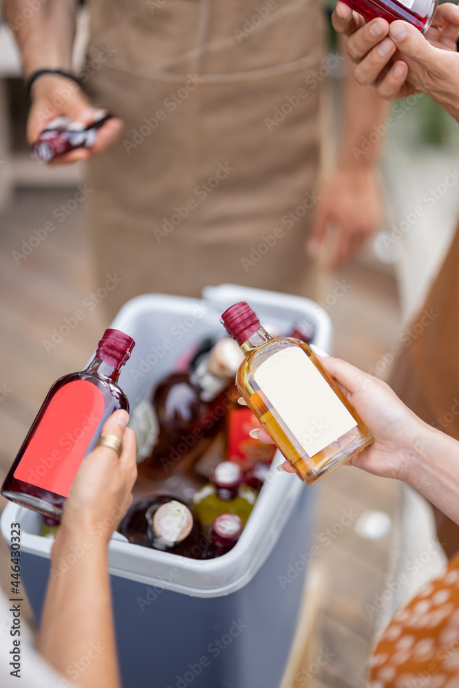 People with alcohol drinks at party outdoors, taking bottles from a fridge, close-up. Bottles with b