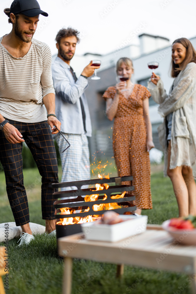 Friends have a picnic, making fire at barbeque, talking and drinking wine on the green lawn at backy