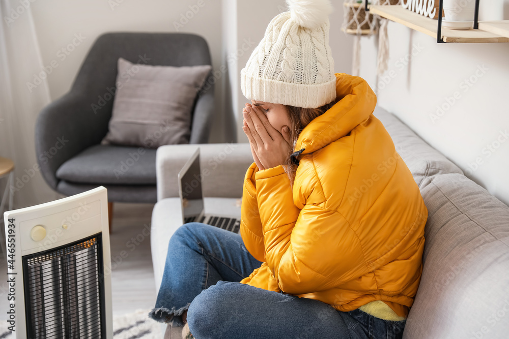 Young woman sitting near electric heater at home. Concept of heating season