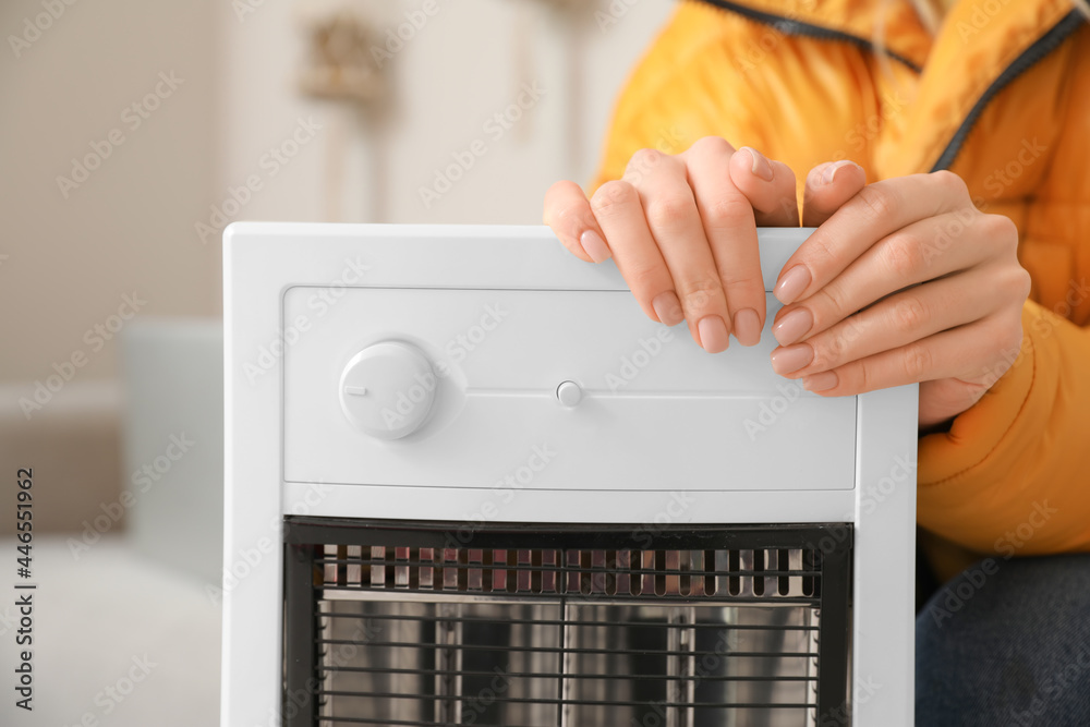 Young woman warming hands near electric heater at home. Concept of heating season