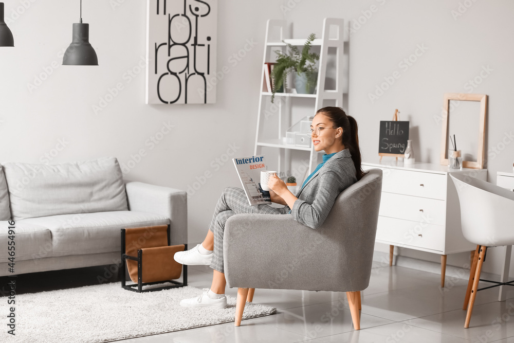 Young woman with coffee and magazine sitting in armchair at home