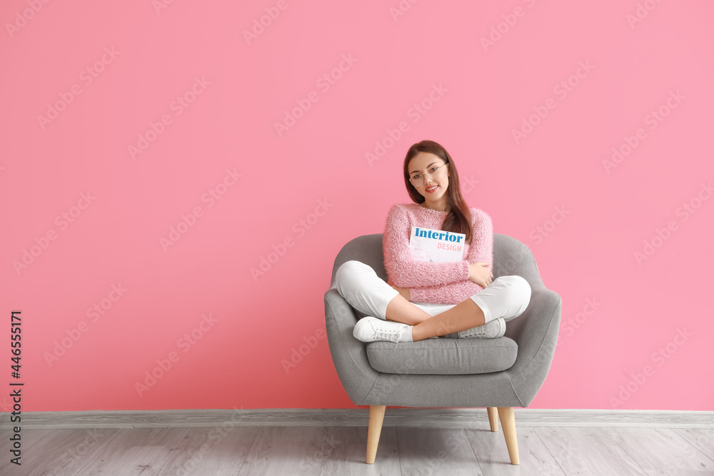 Beautiful young woman sitting in armchair near color wall