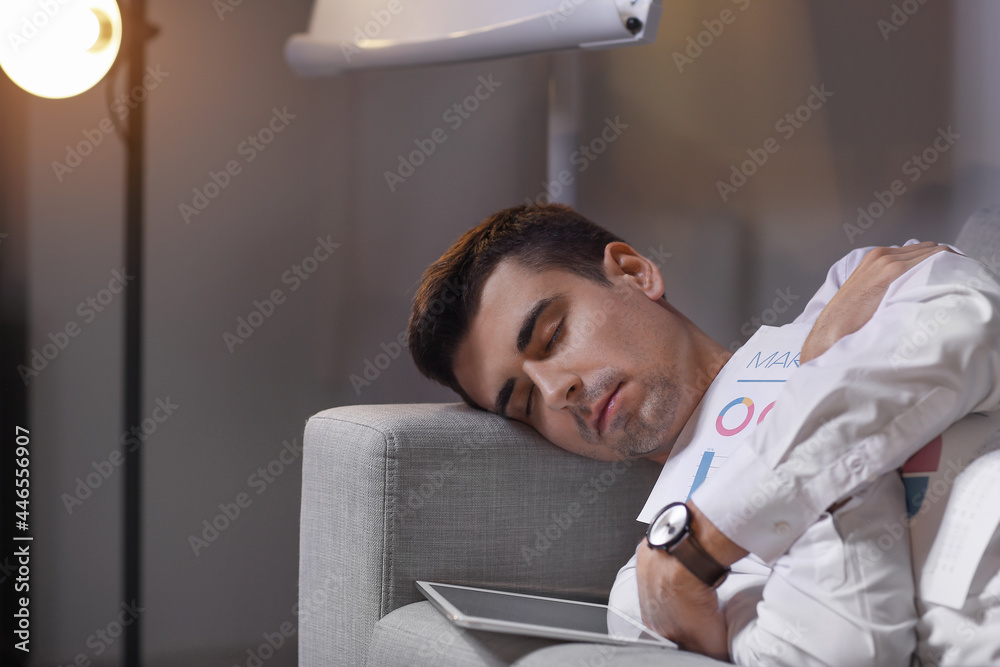 Tired businessman sleeping on sofa in office late at night