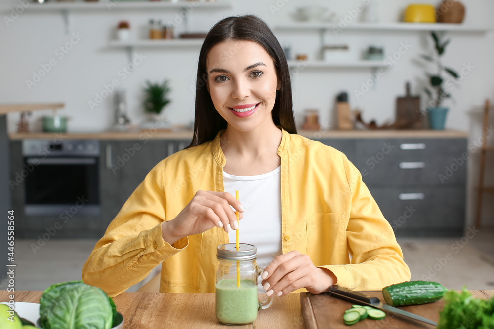 Young woman with glass of healthy green smoothie in kitchen