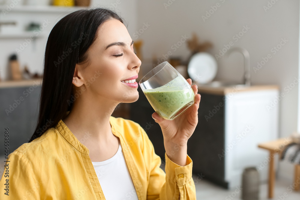 Young woman drinking healthy green smoothie in kitchen