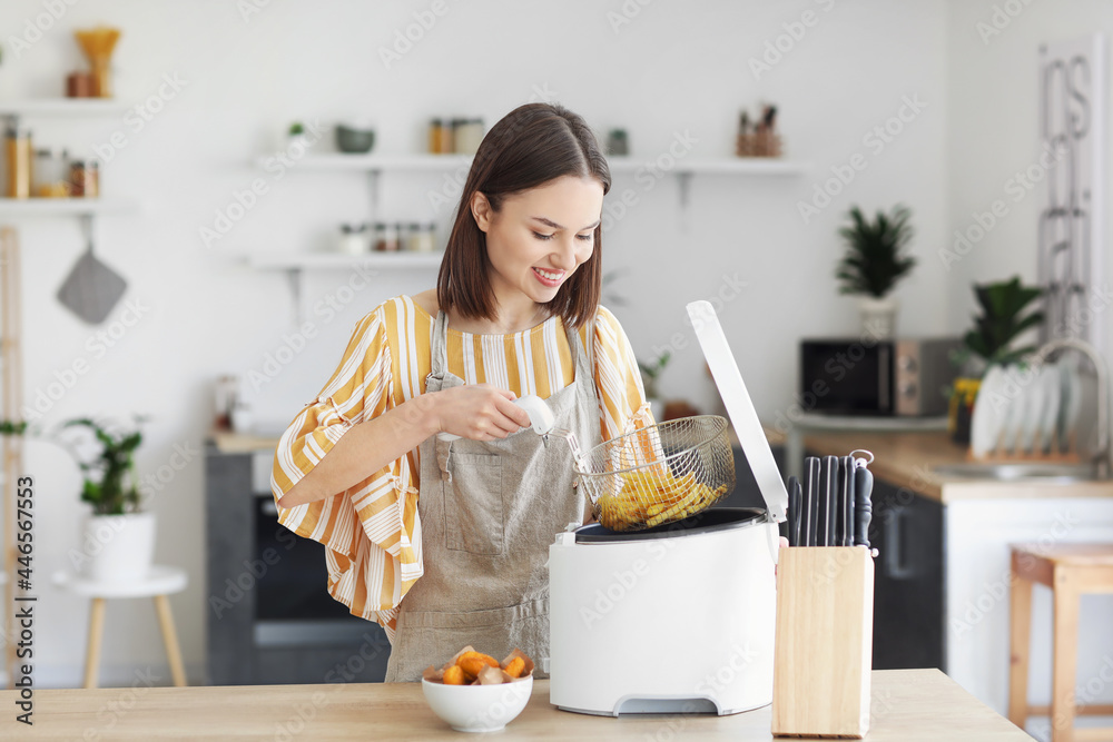 年轻女子在厨房里从油炸锅里取出美味的薯条