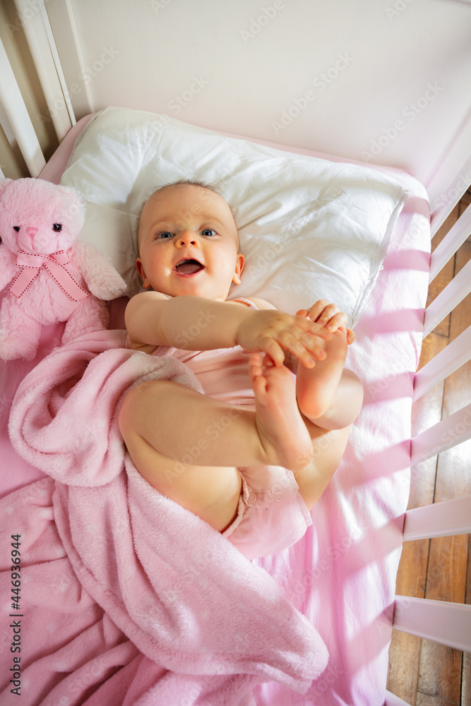 Baby girl lay in pink bed touching legs laughing