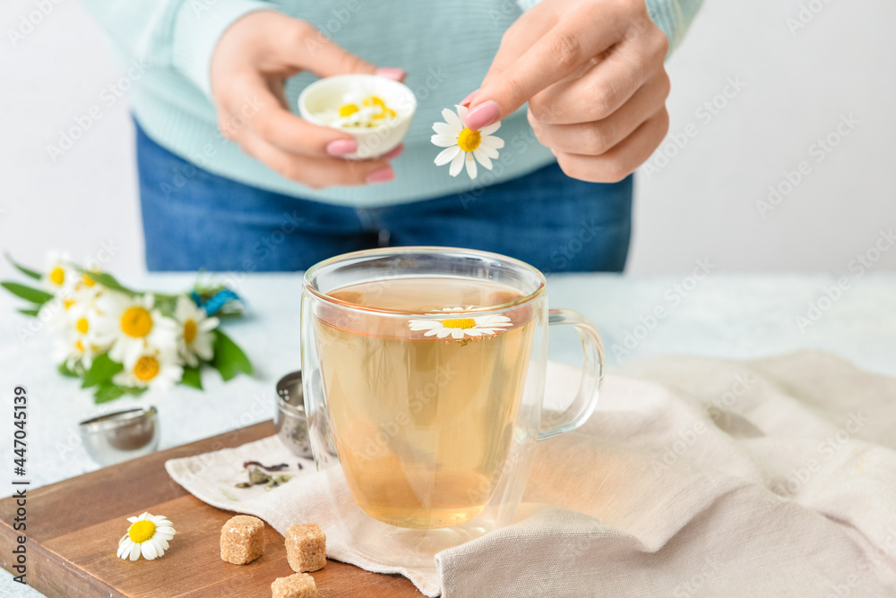 女人把洋甘菊花放进杯子里，桌子上放着茶