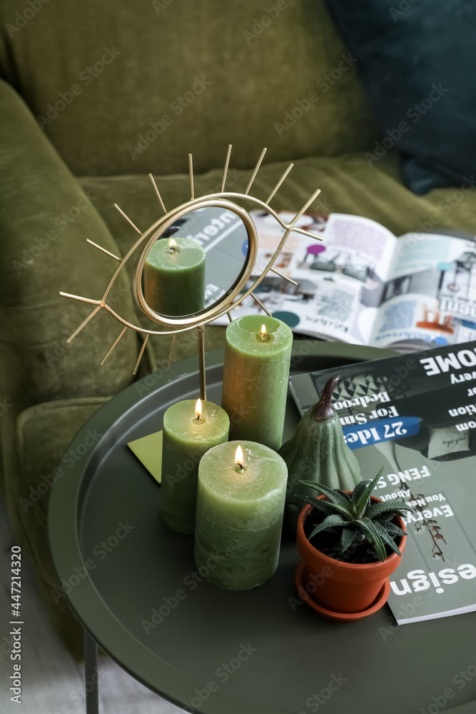 Burning candles, mirror, magazine and houseplant on table in room