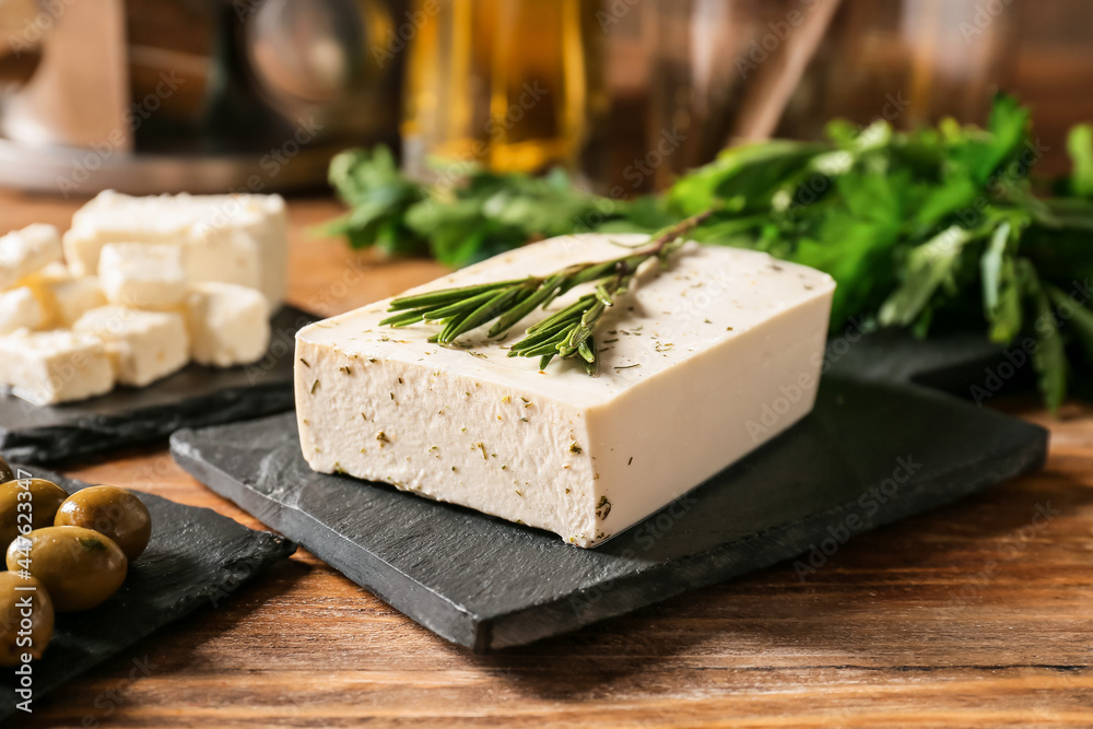 Slate board with tasty feta cheese, olives and rosemary on wooden background, closeup