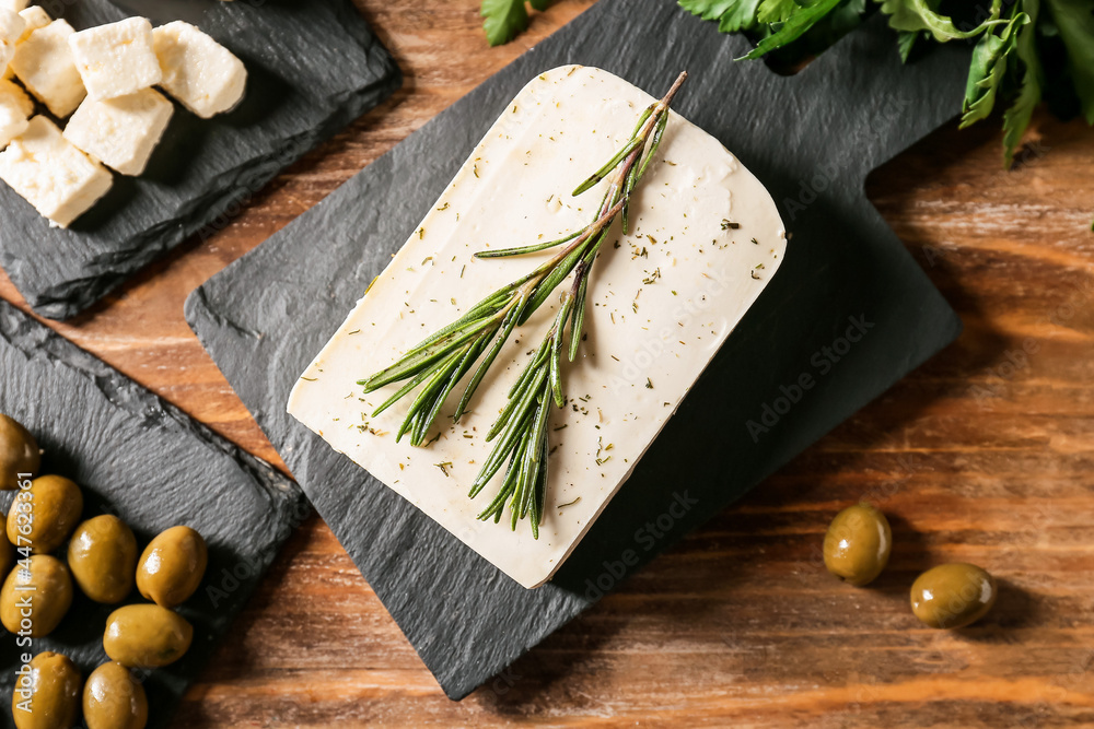 Slate board with tasty feta cheese, olives and rosemary on wooden background, closeup