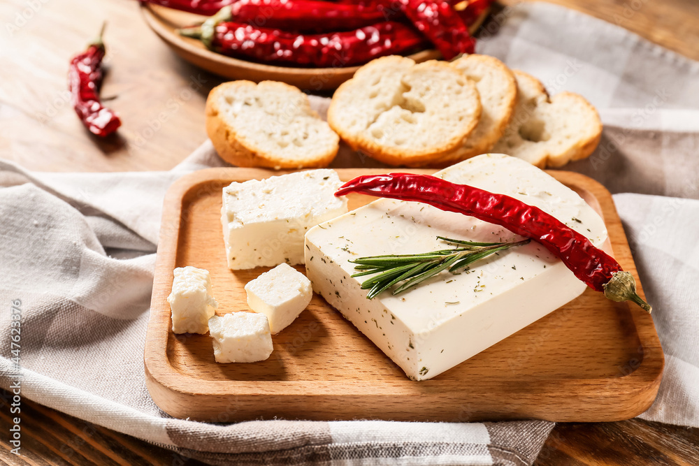 Board with tasty feta cheese, chili pepper and bread on wooden background