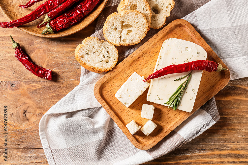 Board with tasty feta cheese, chili pepper and bread on wooden background