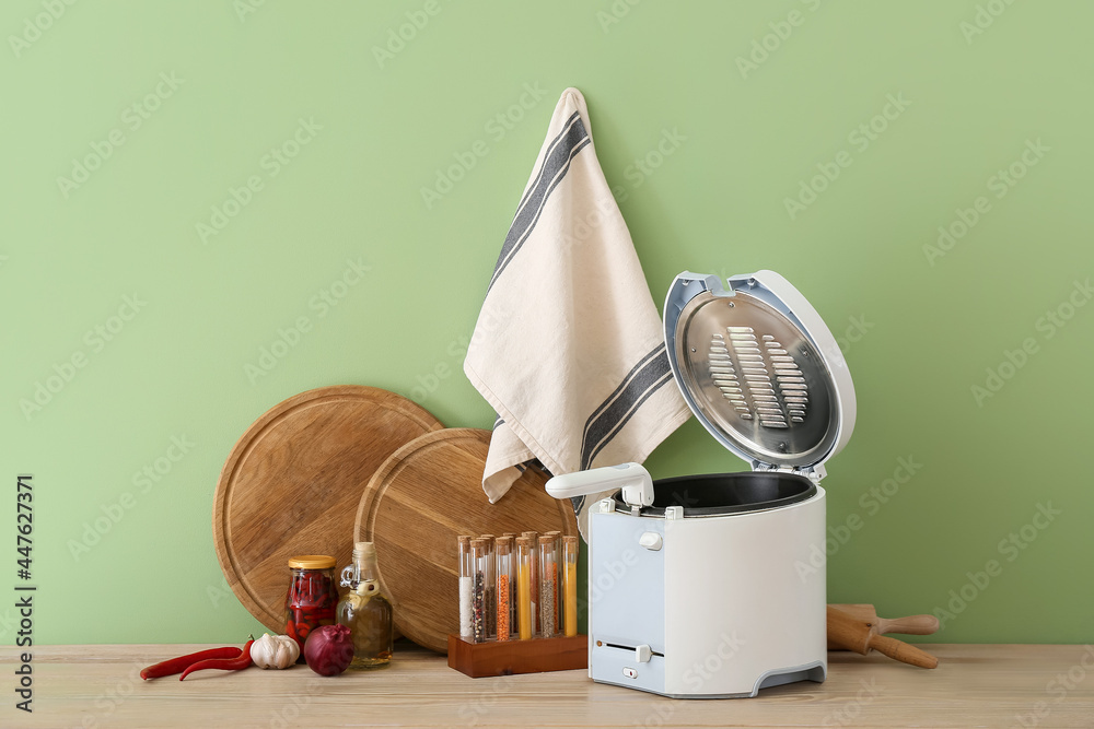 Modern deep fryer on table near color wall