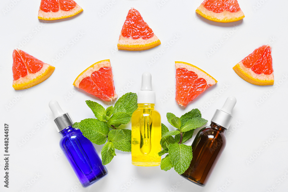 Composition with bottles of essential oil, mint and grapefruit slices on light background