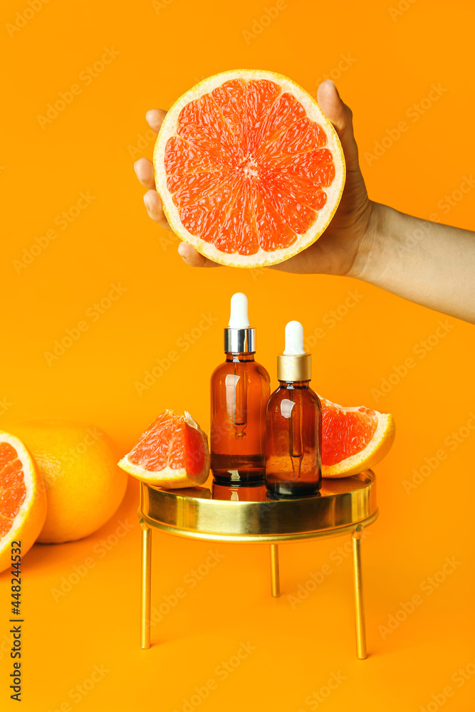 Female hand with grapefruit and bottles of essential oil on color background