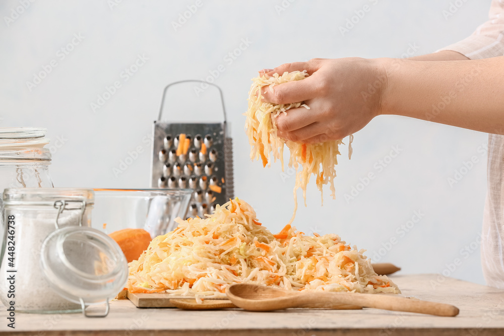 Woman preparing tasty sauerkraut at table in kitchen, closeup