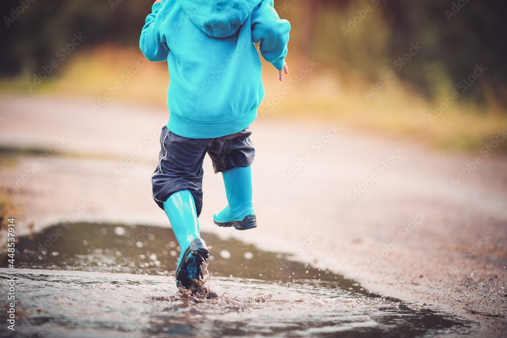 雨天孩子穿着雨鞋在水坑里行走