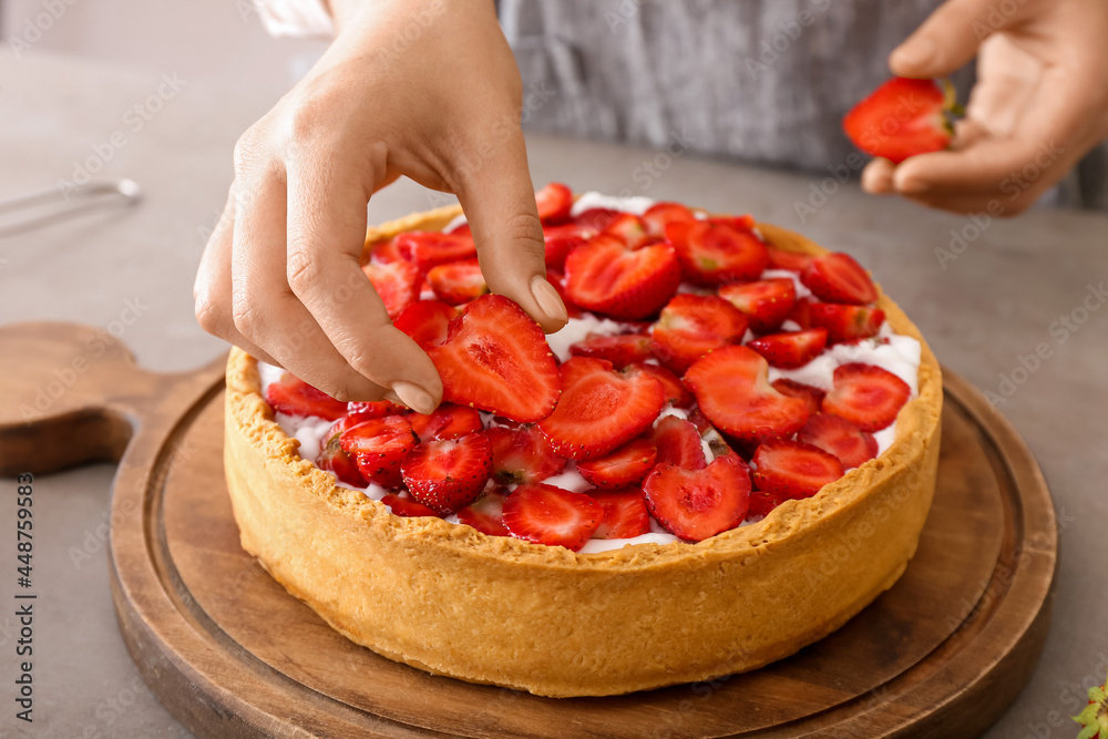 Woman decorating tasty pie with strawberry at table in kitchen, closeup