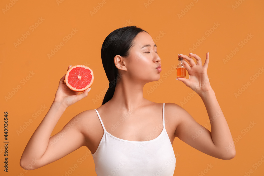 Beautiful young woman with bottle of essential oil and grapefruit on color background